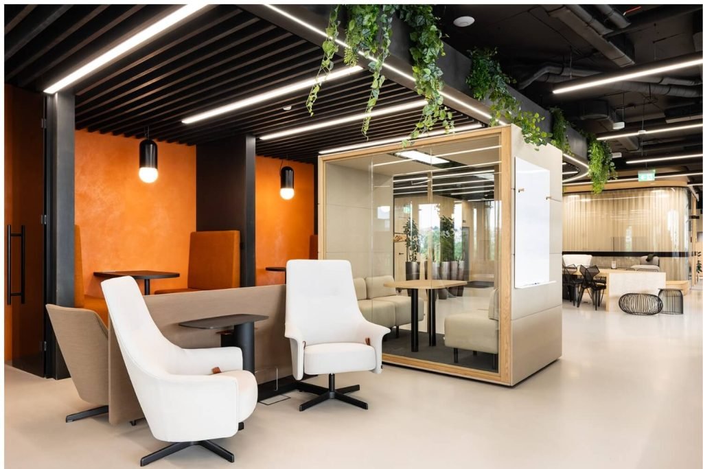 Interior moderno de oficina con cabina insonorizada Chat4 GEN4, sillones, mesas, mamparas de cristal y plantas colgantes