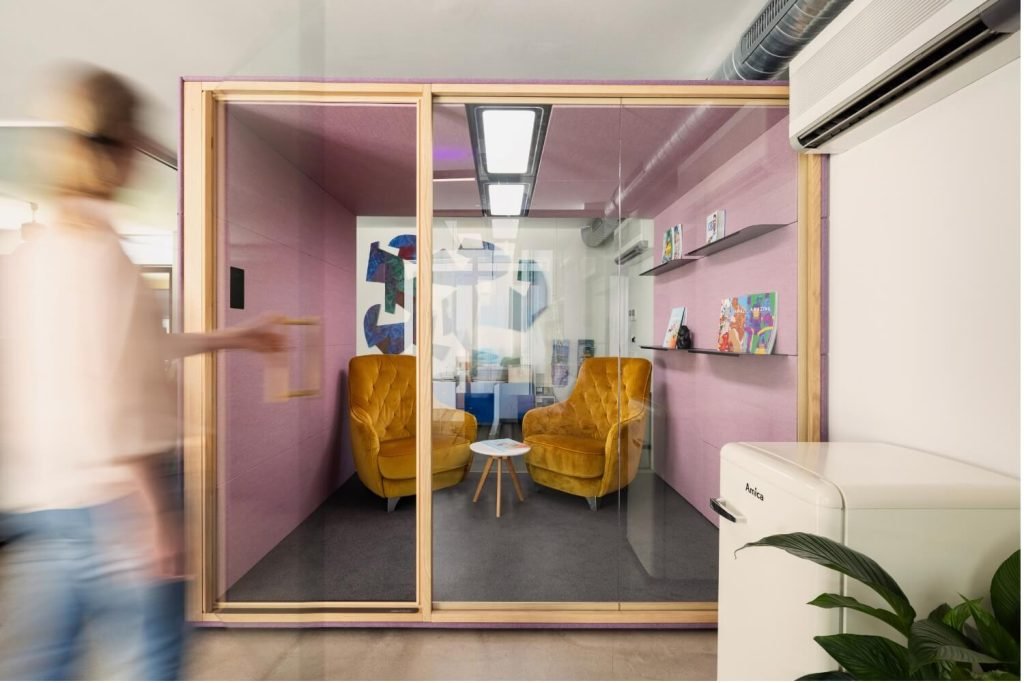 Cabina insonorizada Summit4 GEN4 con dos sillones amarillos, una mesa pequeña y estanterías con libros en una oficina