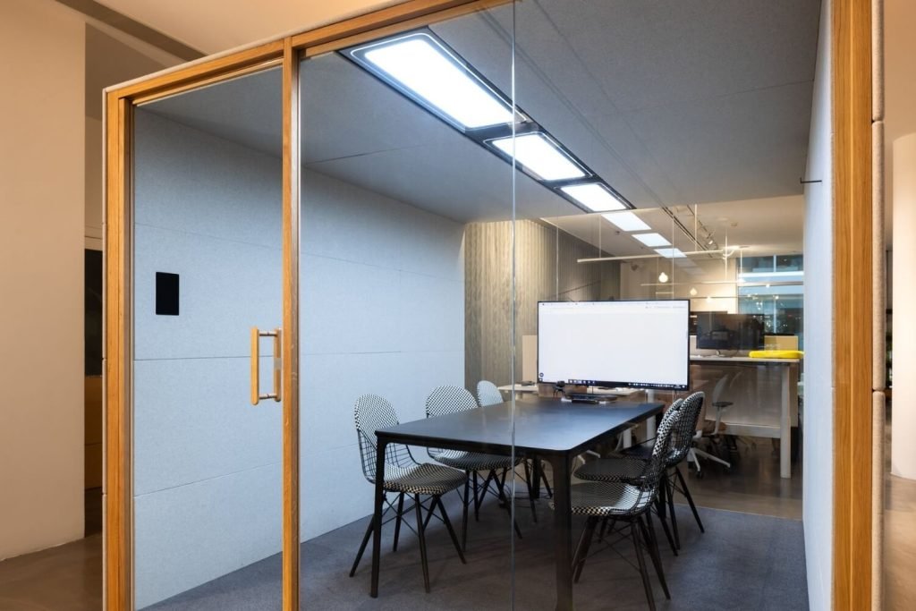 Detalles del interior de una cabina acústica Summit6 GEN4 con mesa, sillas y pantalla grande en la pared