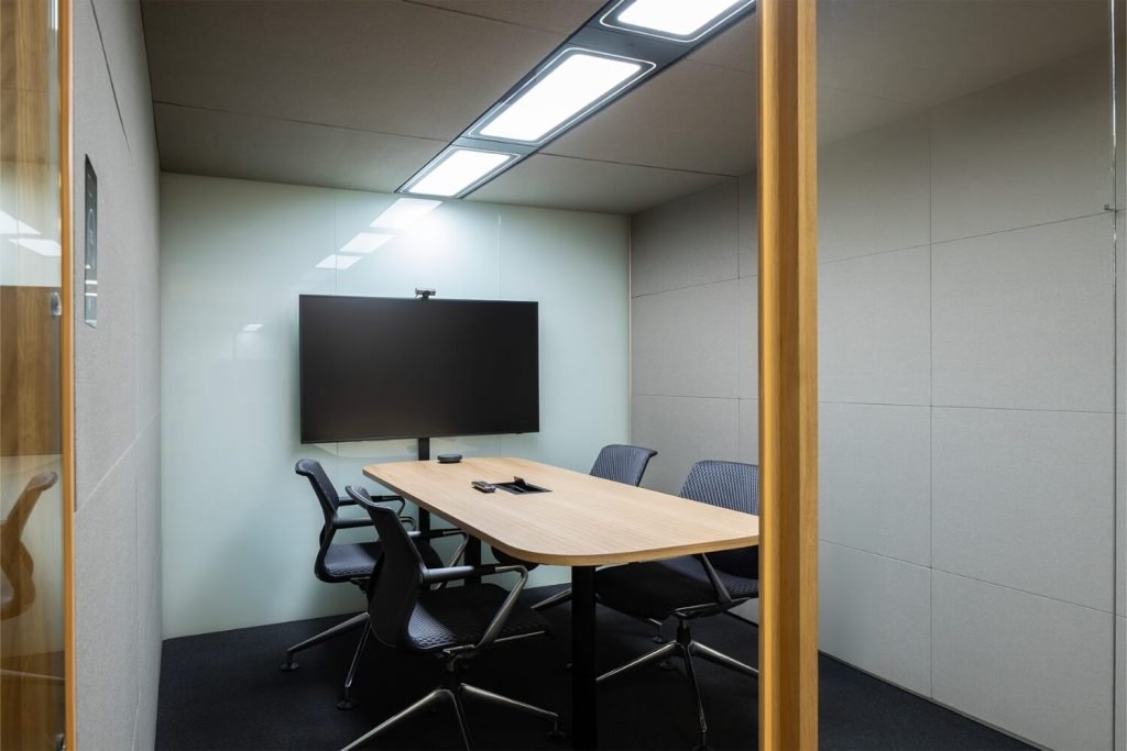 Detalles del interior de una cabina acústica Summit6 GEN4 con mesa, sillas y pantalla grande en la pared