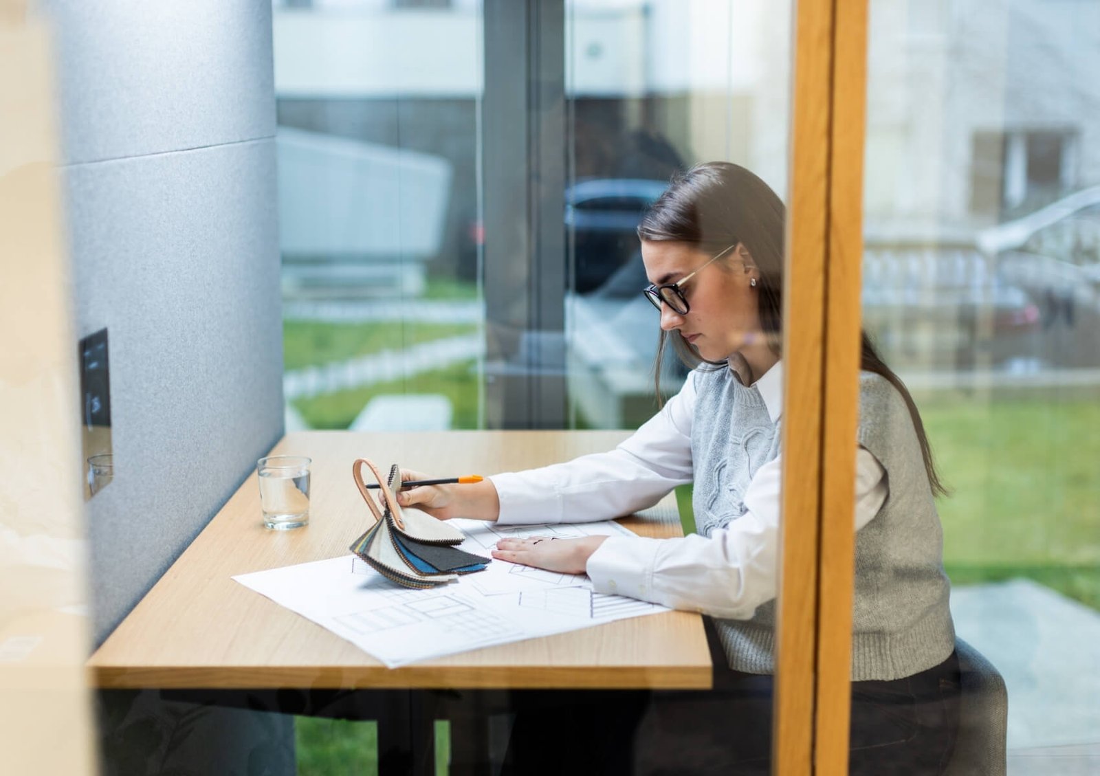 Mujer diseñando sobre planos en una mesa, con muestras de materiales y un lápiz dentro de una cabina acústica Focus GEN4