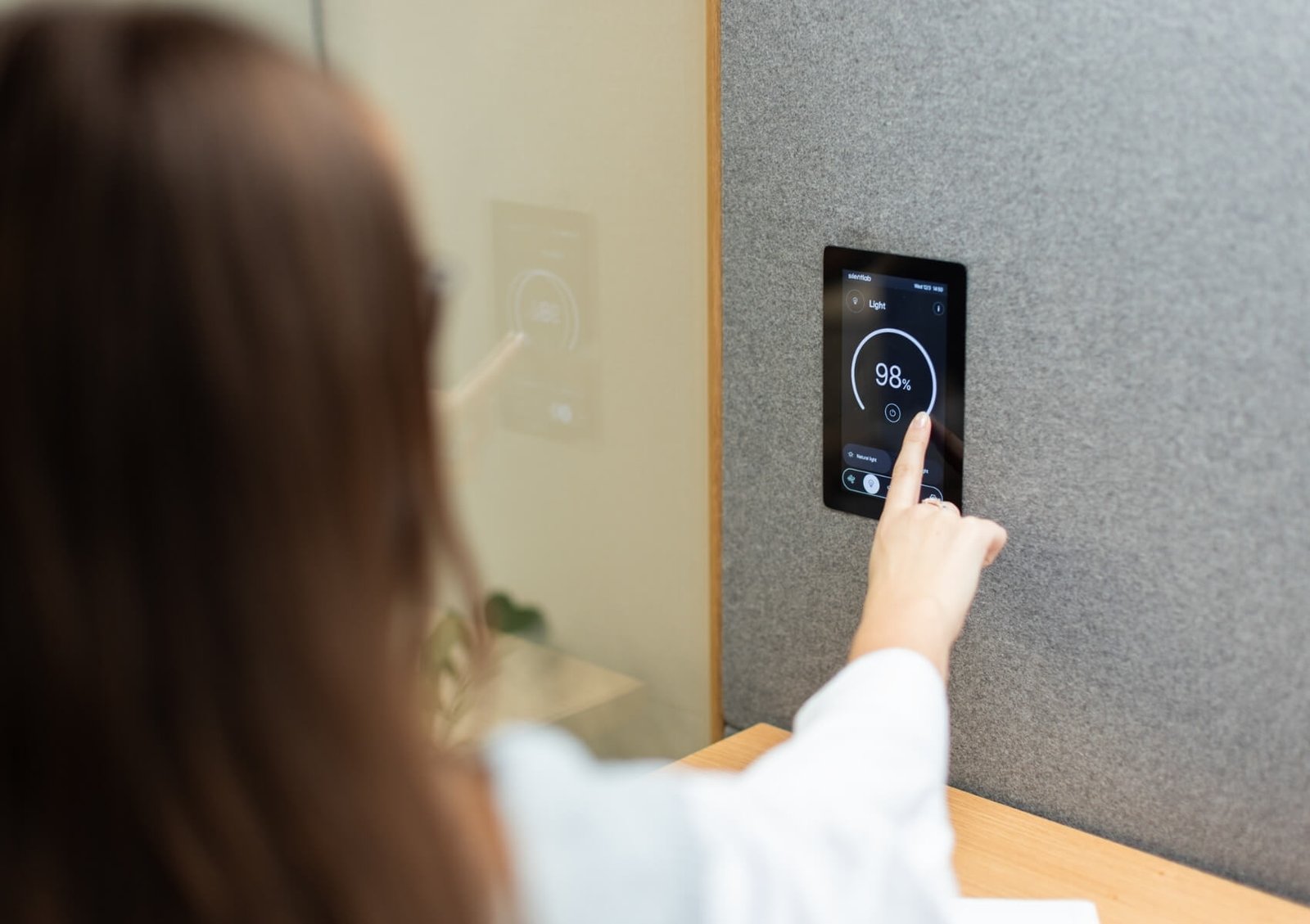 Una mujer toca un panel inteligente de pared que muestra la iluminación al 98 % en un cabina acústica GEN4