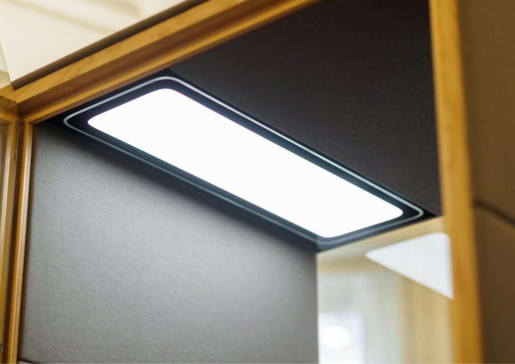 Lámpara LED rectangular instalada en un techo oscuro enmarcado en madera. Detalle interior de una cabina acústica Spot GEN4