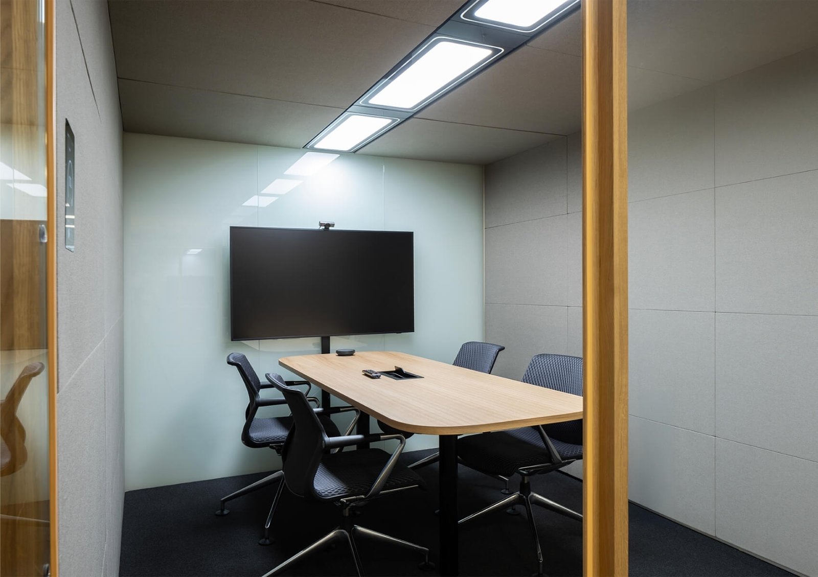 Detalles del interior de una cabina acústica Summit6 GEN4 con mesa, sillas y pantalla grande en la pared