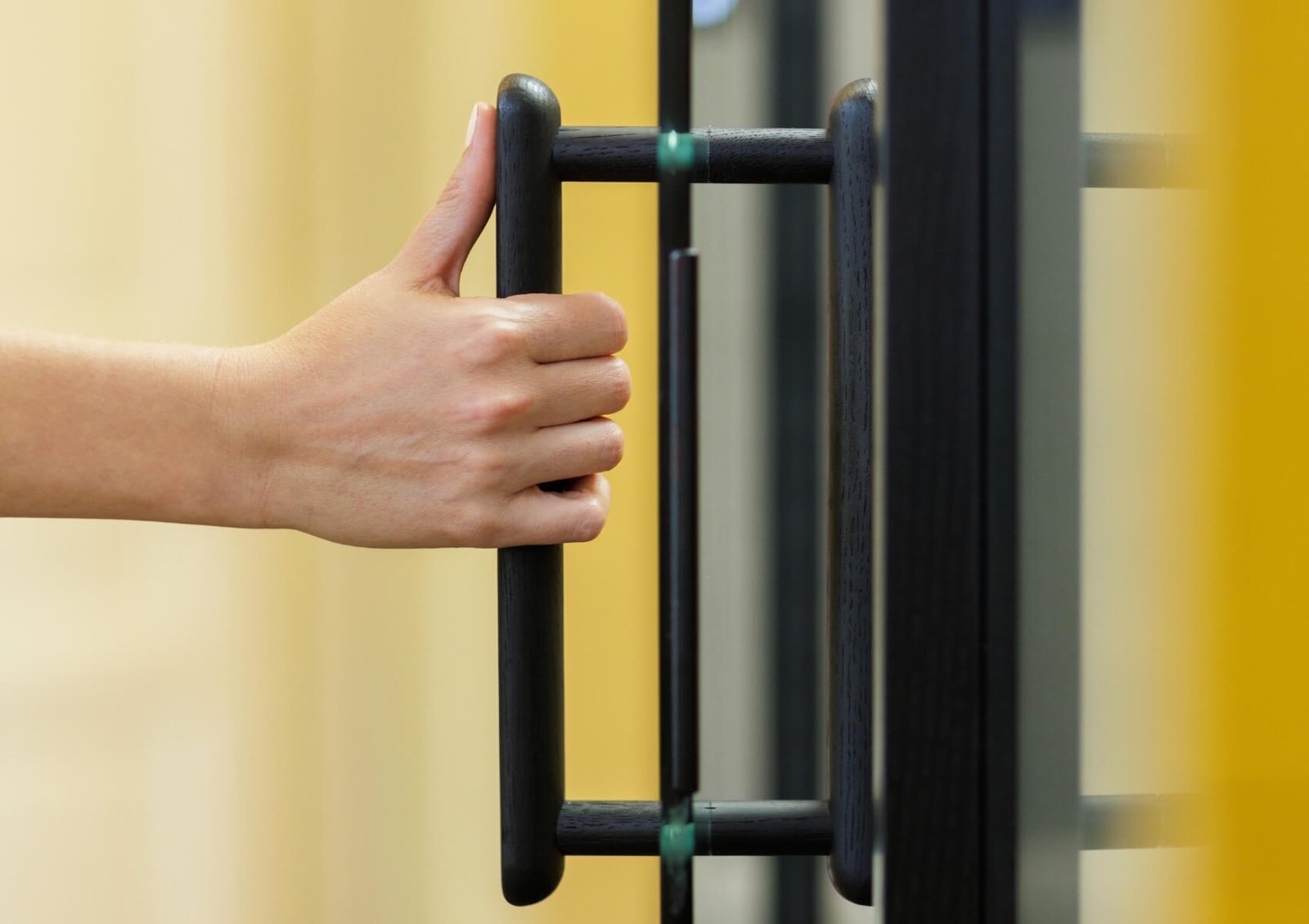 Una mano abre una puerta de cristal con un tirador negro de una cabina acústica GEN4
