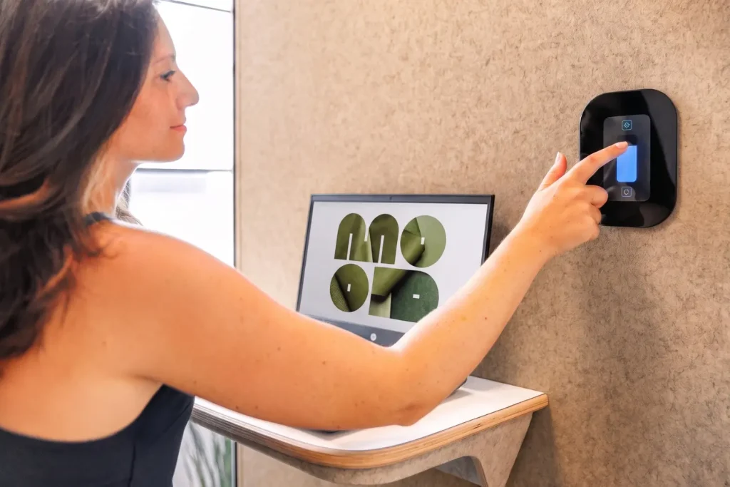 Mujer pulsando la pantalla táctil de un dispositivo de control fijado a la pared de una cabina acústica MOOD Phone