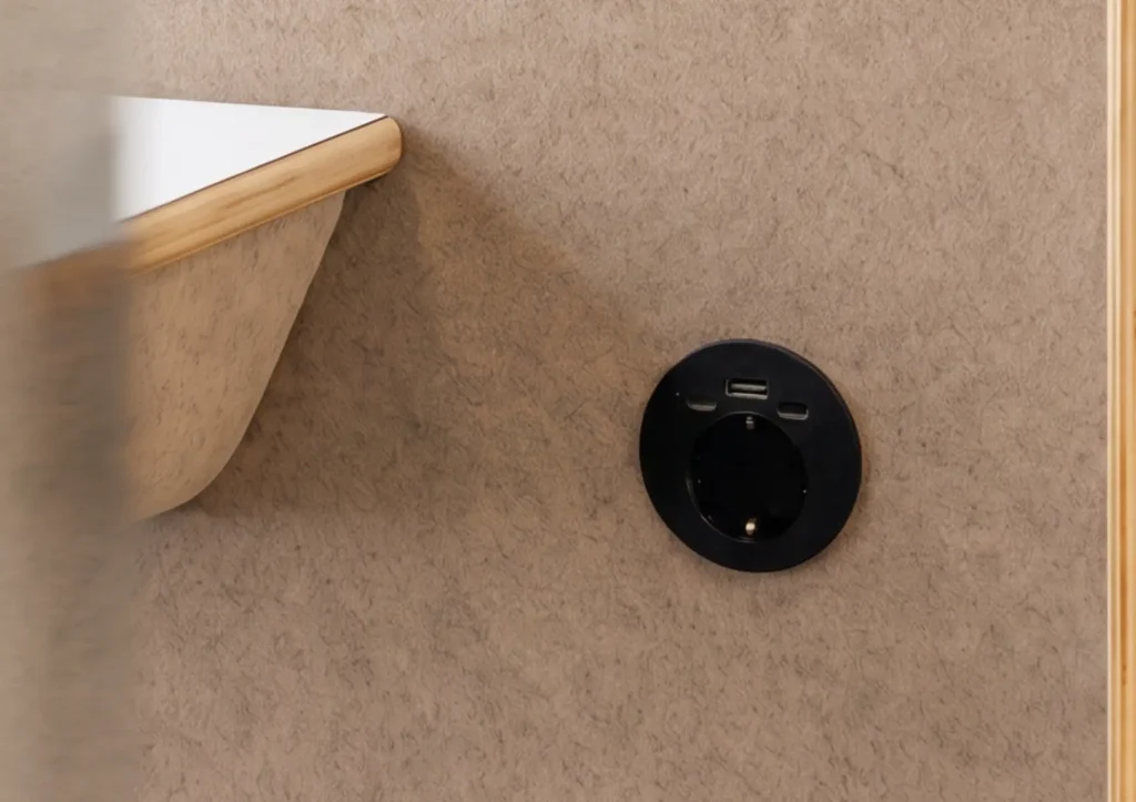 Toma de corriente eléctrica negra con puerto USB integrada en una cabina acústica MOOD Phone