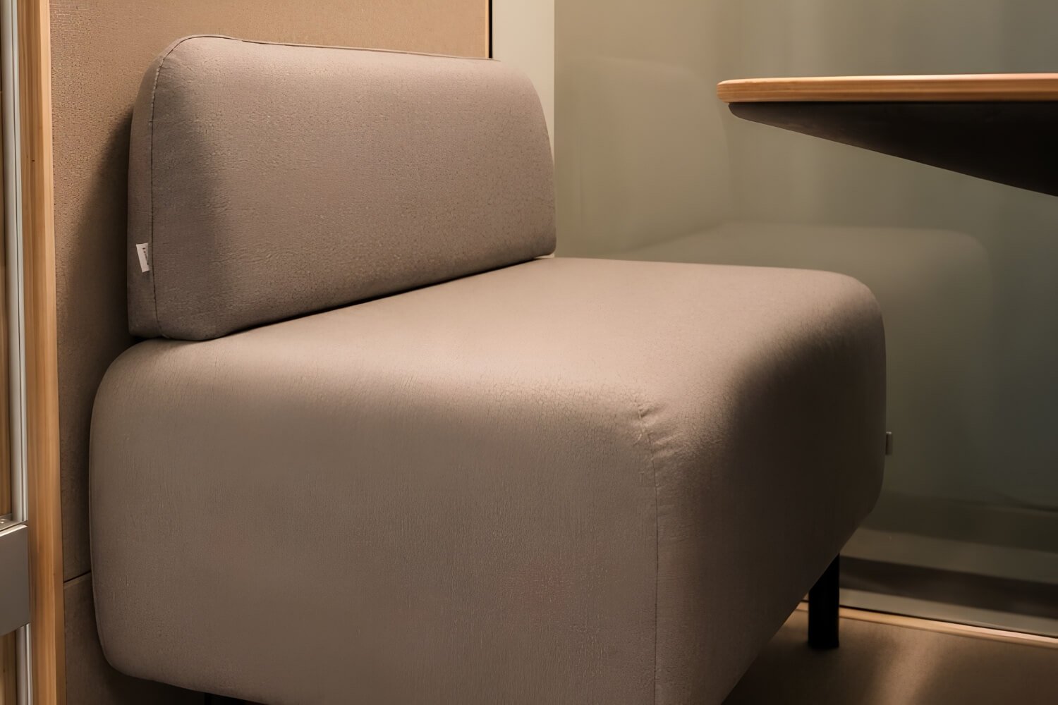 Sillón tapizado beige con respaldo redondeado, en un interior junto a mesa de trabajo. Interior de una cabina acústica MOOD hybrid