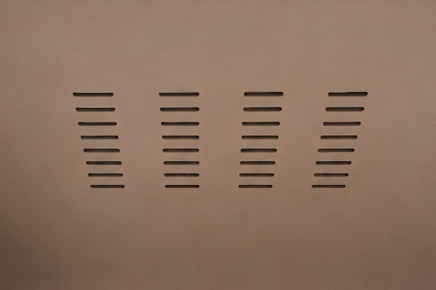 Cuatro columnas de ranuras horizontales de ventilación en una pared de color beige. Detalle interior de una cabina acústica MOOD Meet