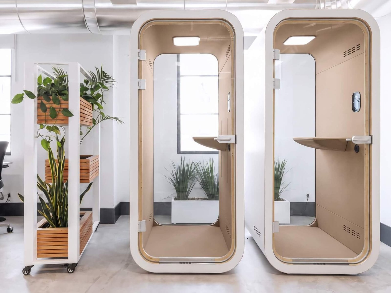 Dos cabinas acústicas MOOD Phone de oficina con puertas abiertas, junto a un separador móvil con plantas